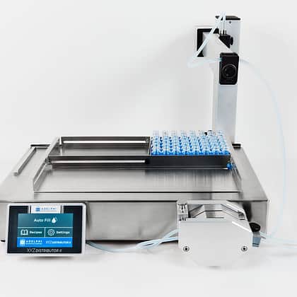 Adelphi Manufacturing XYZ Distributor II with full front angled view, featuring stainless steel conveyor, blue capsules, touchscreen control panel, and filling system for pharmaceutical dosing and automated production.