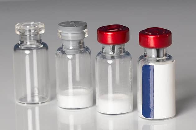 Four vials: one empty, one containing lyophilised powder with a stopper, one containing powder, with a red crimp seal and one sealed and labelled.