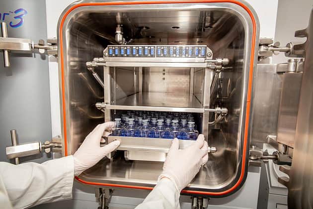 Gloved hands putting a tray of vials into a freeze dryer