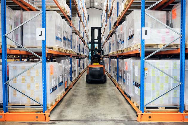 A forklift truck drives between shelves of warehouse racking.