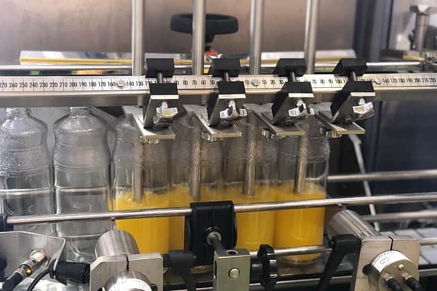 A 4 head filling machine in the middle of filling orange juice in large see through containers from the bottom up.
