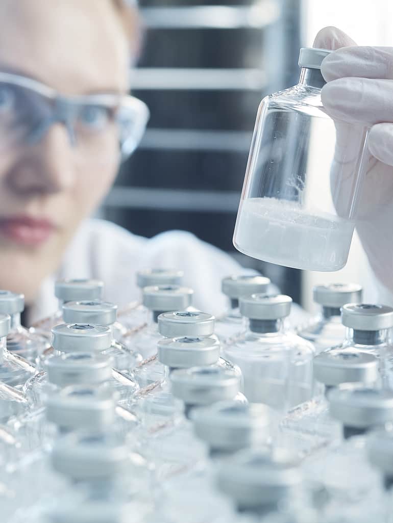 Lab technician inspecting a vial of lyophilised powder.