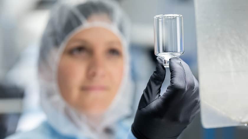A woman in protective gear holding a clear glass vial.