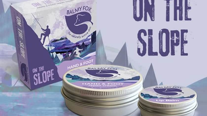 on a puple geometric background is a Balmy Fox product with a purple box and a large and small tin of balm, with purple labels on
