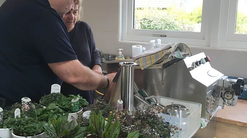 a man and a woman in dark clothing lean over a Response Benchtop Filler, with a selection of plants in a crate beside them on the table top