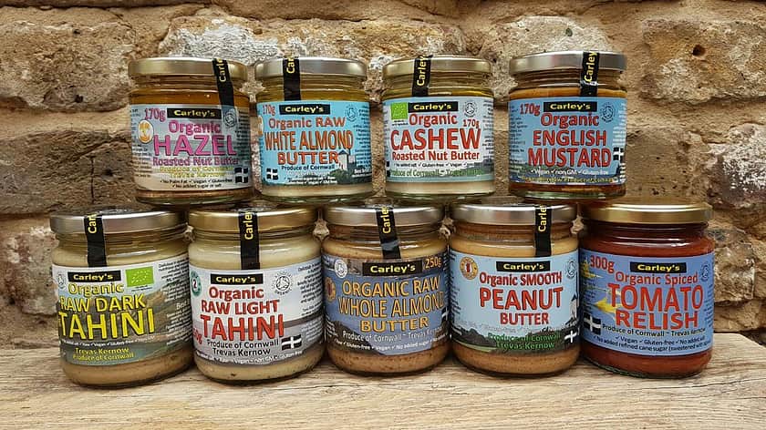 a selection of Carley's of Cornwall products with five glass jars in a row, with four more glass jars stacked on top. All the jars have brightly coloured labels and filled with sauces.