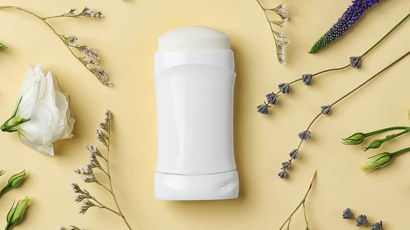 a white deodorant stick lying down on a yellow background with purple and white flowers and stems lying around it
