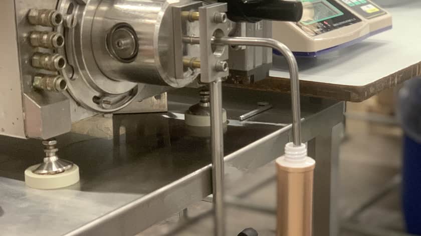 a close up of a filling machine with a slim container underneath the nozzle