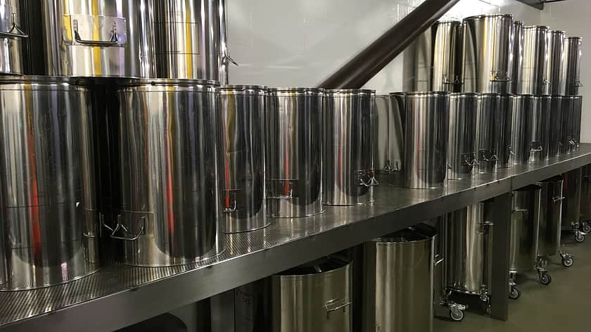 a long line up of large silver metal mixing vessels reaching out into the distance on a metal table
