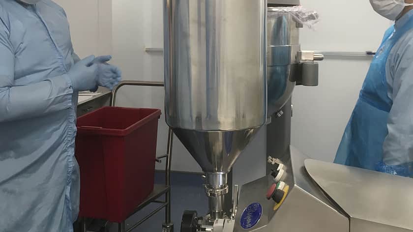 a man and a woman both in blue protective overcoats, with hair nets and face masks standing either side of a large mixing machine