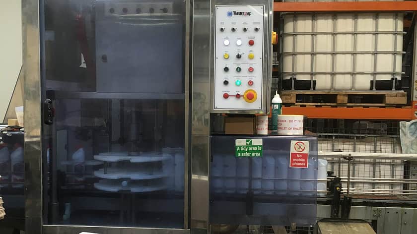 A large factory machine in a factory setting, with a line up of boxes in front of it