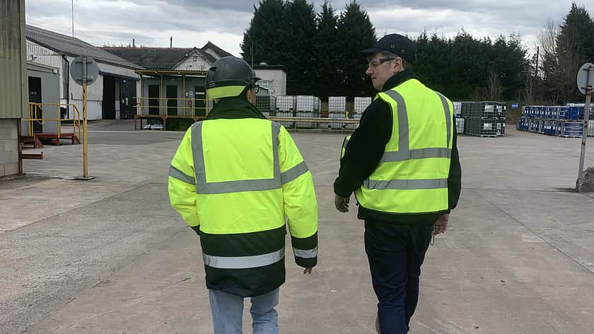 Two people in high-vis jackets talking and walking across a carpark away from the camera