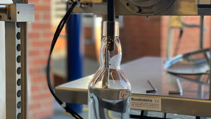 a close up of a nozzle from a filling machine in the top of a glass bottle