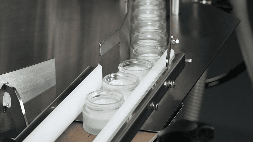 A line of small jars coming out of a conveyor after they have had product filled into them.