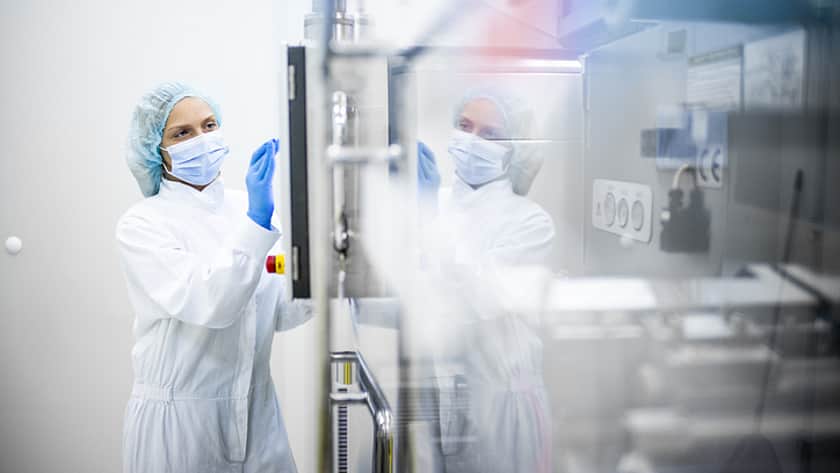 Eine Frau in Schutzkleidung vor einem Isolator.