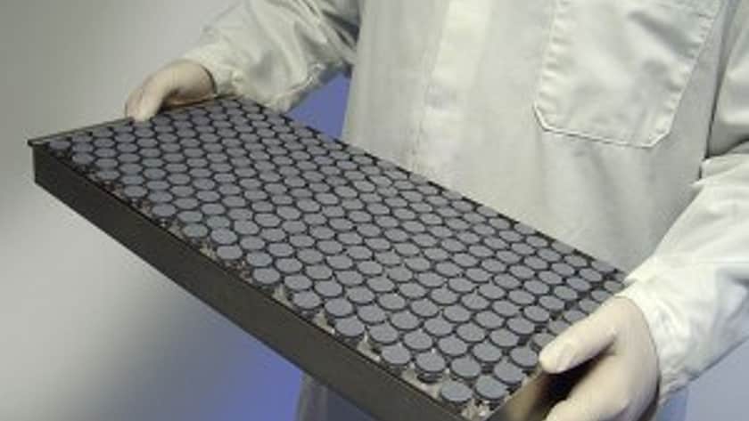 Ein Labortechniker hält ein Metalltablett, das mit verschlossenen Phiolen gefüllt ist.