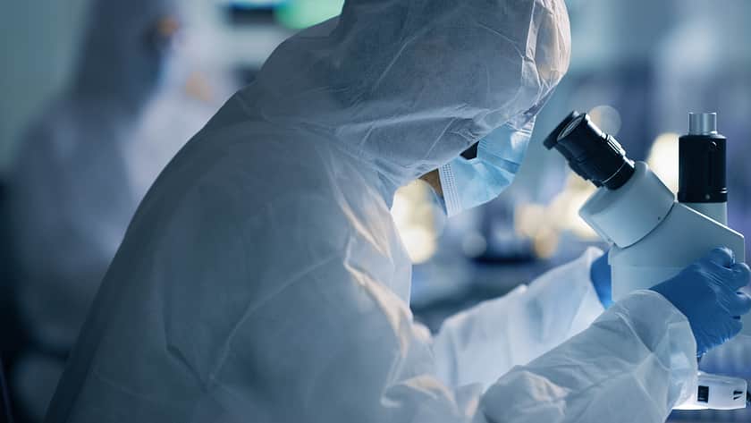 Anzugtragender Labortechniker blickt ins Mikroskop