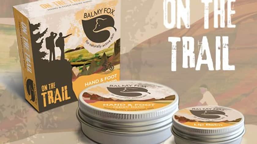 on a beige geometric background is a Balmy Fox product with a beige box and a large and small tin of balm, with beige labels on