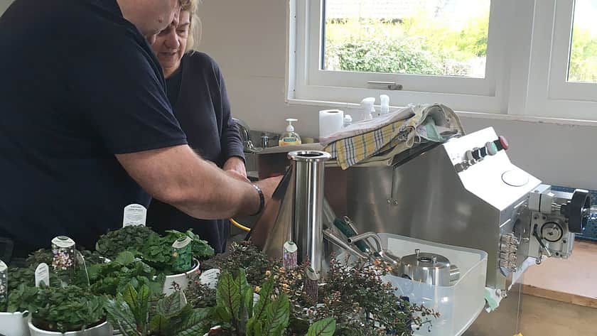 a man and a woman in dark clothing lean over a Response Benchtop Filler, with a selection of plants in a crate beside them on the table top
