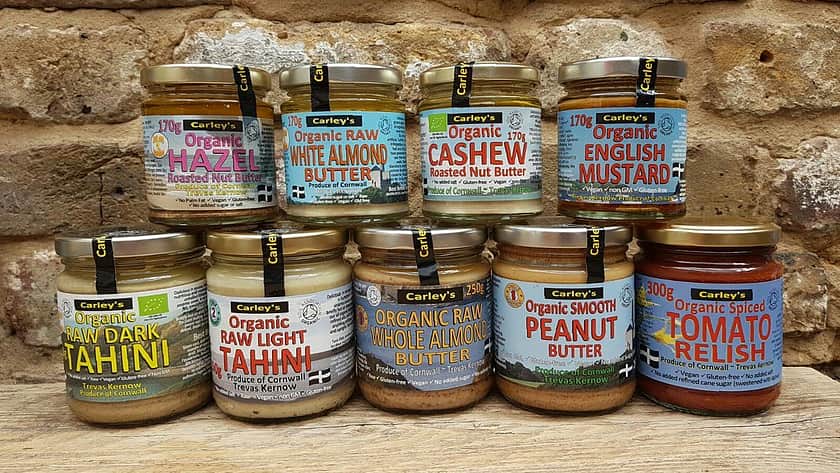 a selection of Carley's of Cornwall products with five glass jars in a row, with four more glass jars stacked on top. All the jars have brightly coloured labels and filled with sauces.