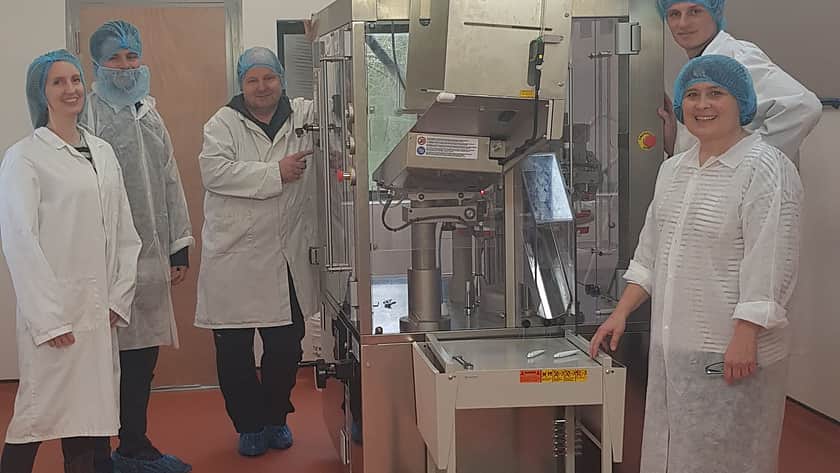 a group of people in white lab coats with blue hair nets gather around a large factory machine all looking at the camera