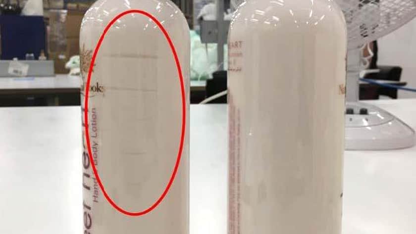 two large clear bottles with brown lids standing next to each other with a red circle drawn over one. The one with the red circle has marks on the bottle from the nozzle