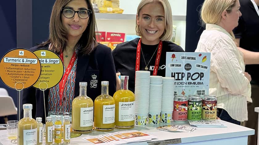 Trade show stand with visitors behind a display of bottled juices, featuring branded counter and packaged products, highlighting food and beverage sampling, product promotion, and industry exhibition.