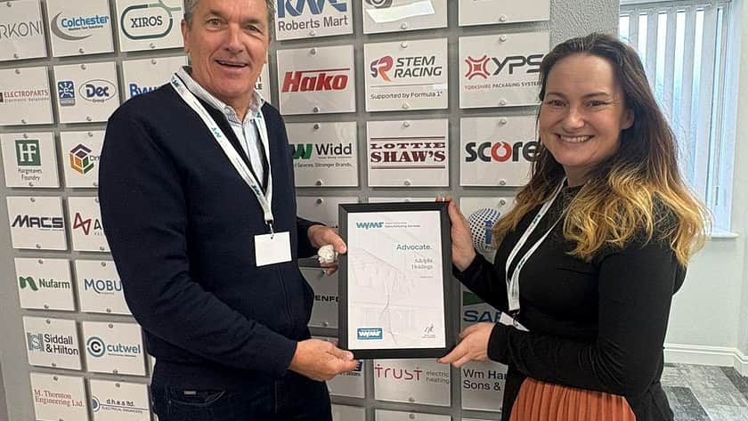 Two people stand in front of a wall of logos on white background, then man handing over a certificate to a smiling woman, both looking at the camera