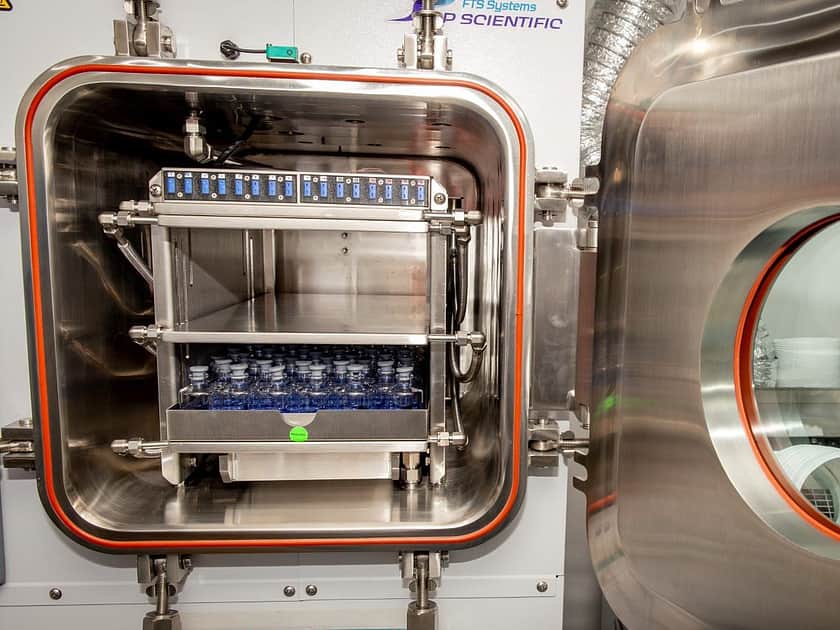 A small freeze drying machine with it's door open and trays of vials inside.