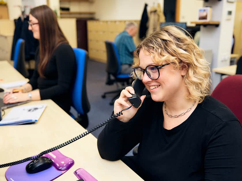 Eine lächelnde Frau in einem Büro, die am Telefon spricht.