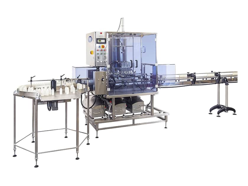 A large factory filling machine on a white background. The machine is metal, with a flat surface on the lefthand side, with a number of small white containers standing on it, to then be filtered into the larger box area in the middle of the machine. The large central part has a blue tint screen around complicated mechanisms, where the filling takes place. On the righthand side of the box area is a slim mechanical belt, where the containers will end up in a neat line, to go onto the next step of the process.