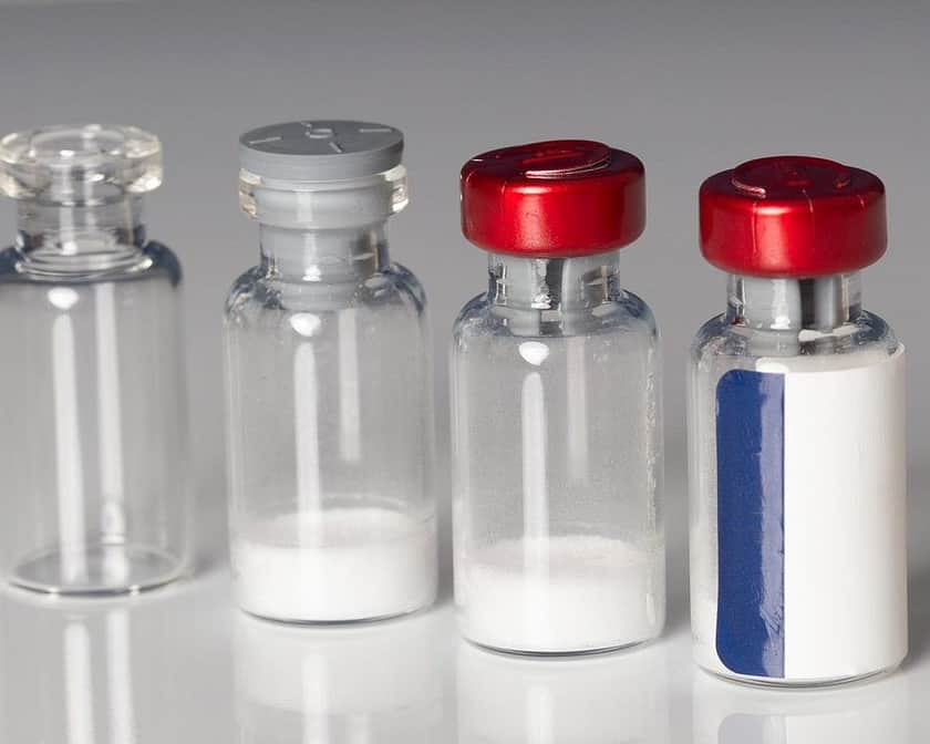 Vier Fläschchen: eines leer, eines mit lyophilisiertem Pulver und einem Stopfen, eines mit Pulver und rotem Bördelverschluss und eines versiegelt und etikettiert.