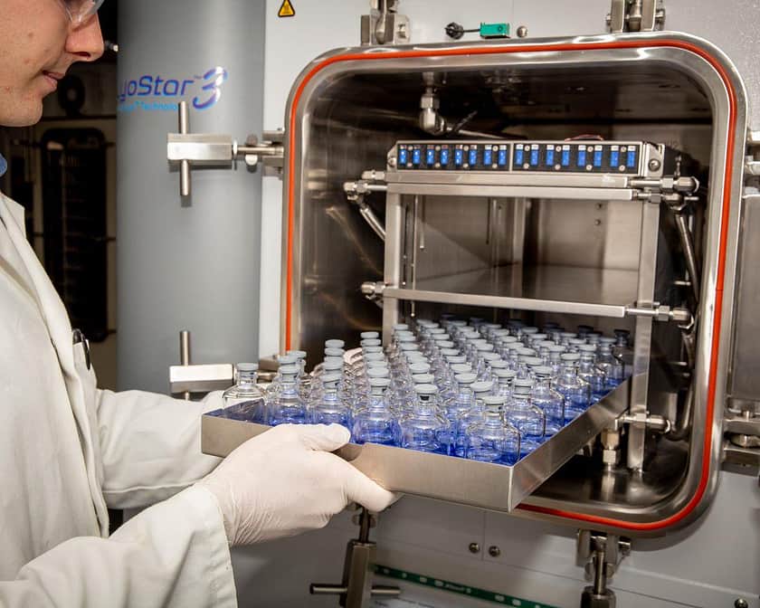 A young male lab technician placing a tray of vials into a lyophiliser.