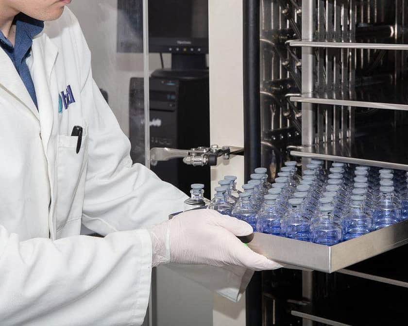A lab technicial placing a sliver tray of vials into a freeze dryer.