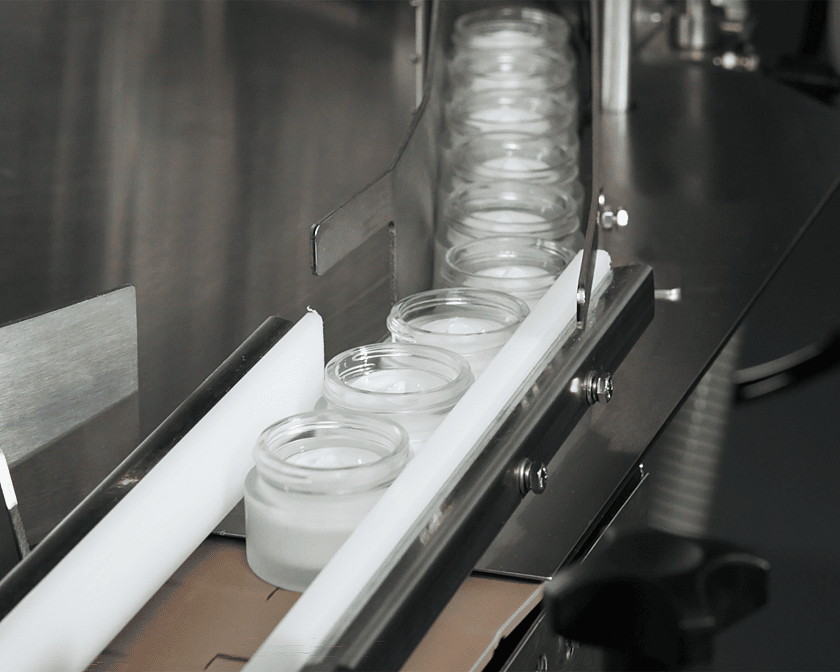 A line of small jars coming out of a conveyor after they have had product filled into them.