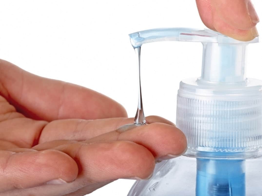 a close up of a hand at a hand sanitiser bottle pump, with hand sanitiser coming out of the spout