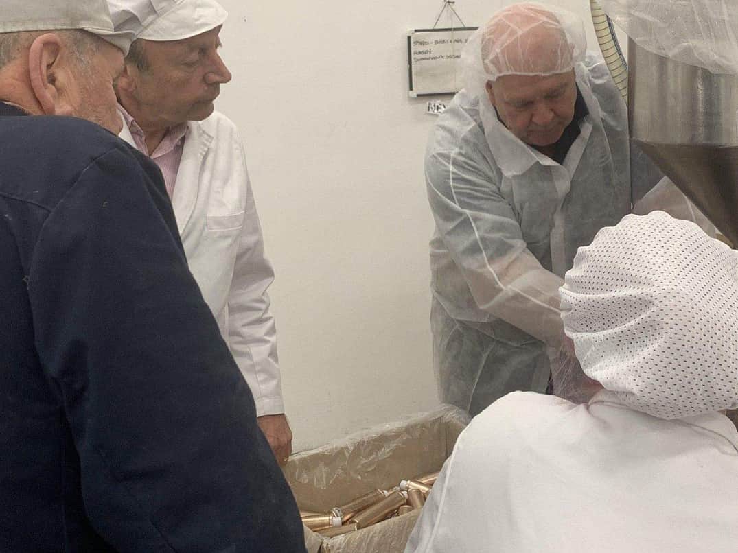 A group of four people, all in white lab coats and hair nets, crowd around a Response Benchtop Filler