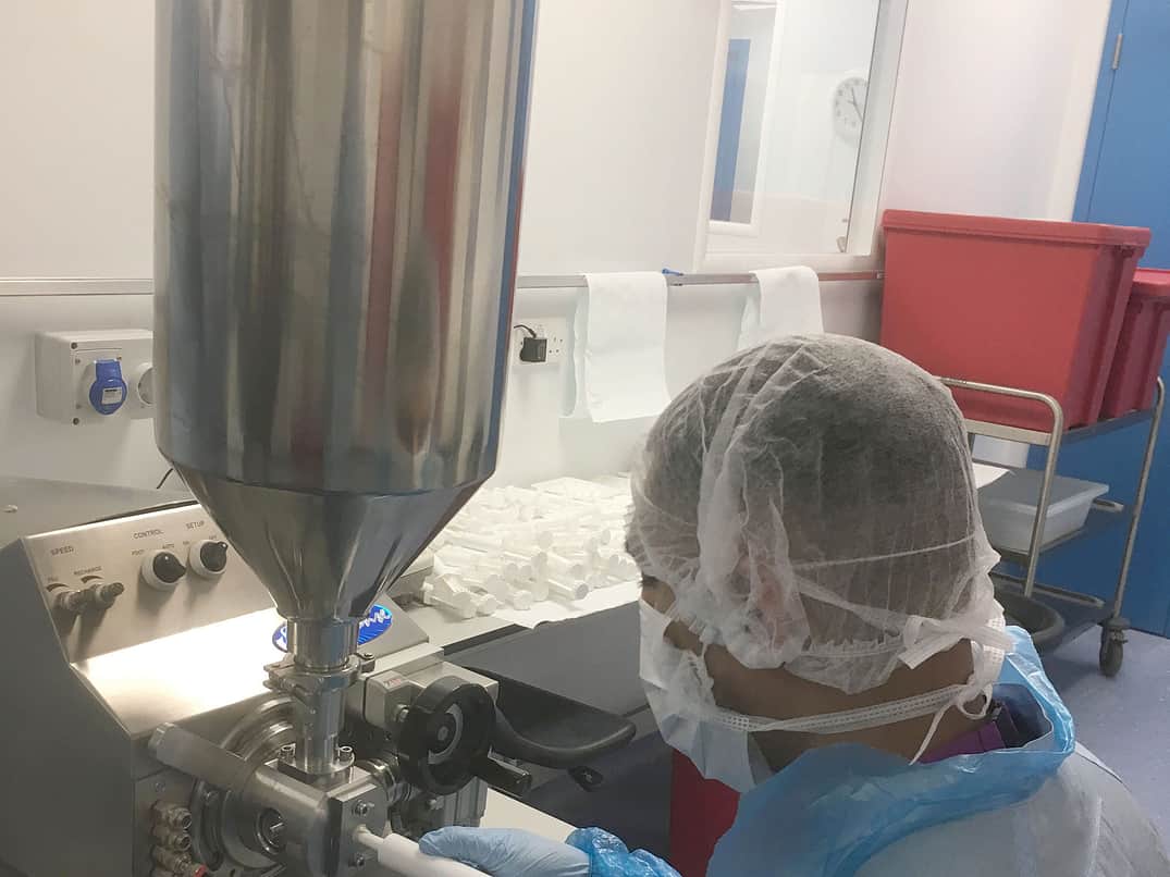 a person with a blue protective overcoat, a hairnet and face mask sits in front of a Response Benchtop filler