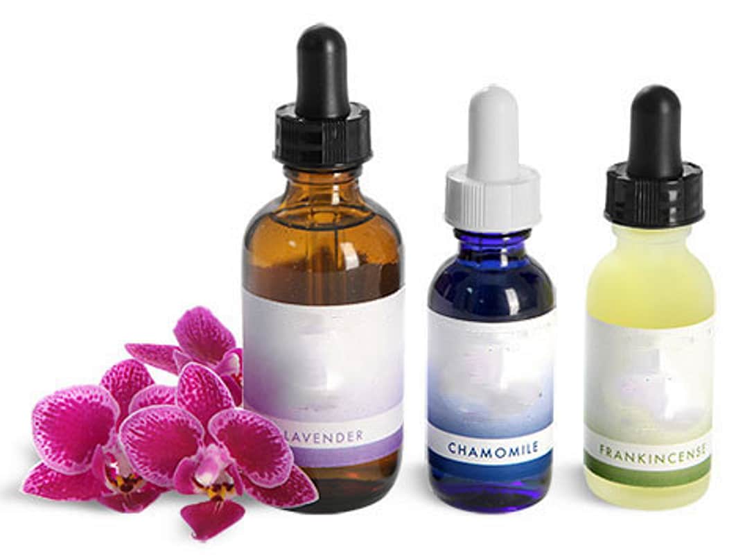 three serum / facial oil dropper bottles on a white background, with a bright pink flower leaning on the largest bottle on the left