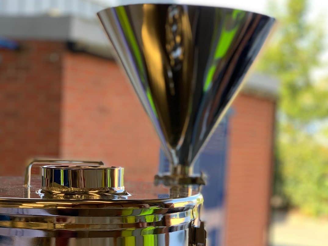 a close up of a silver metal funnel going into the top of a metal vessel