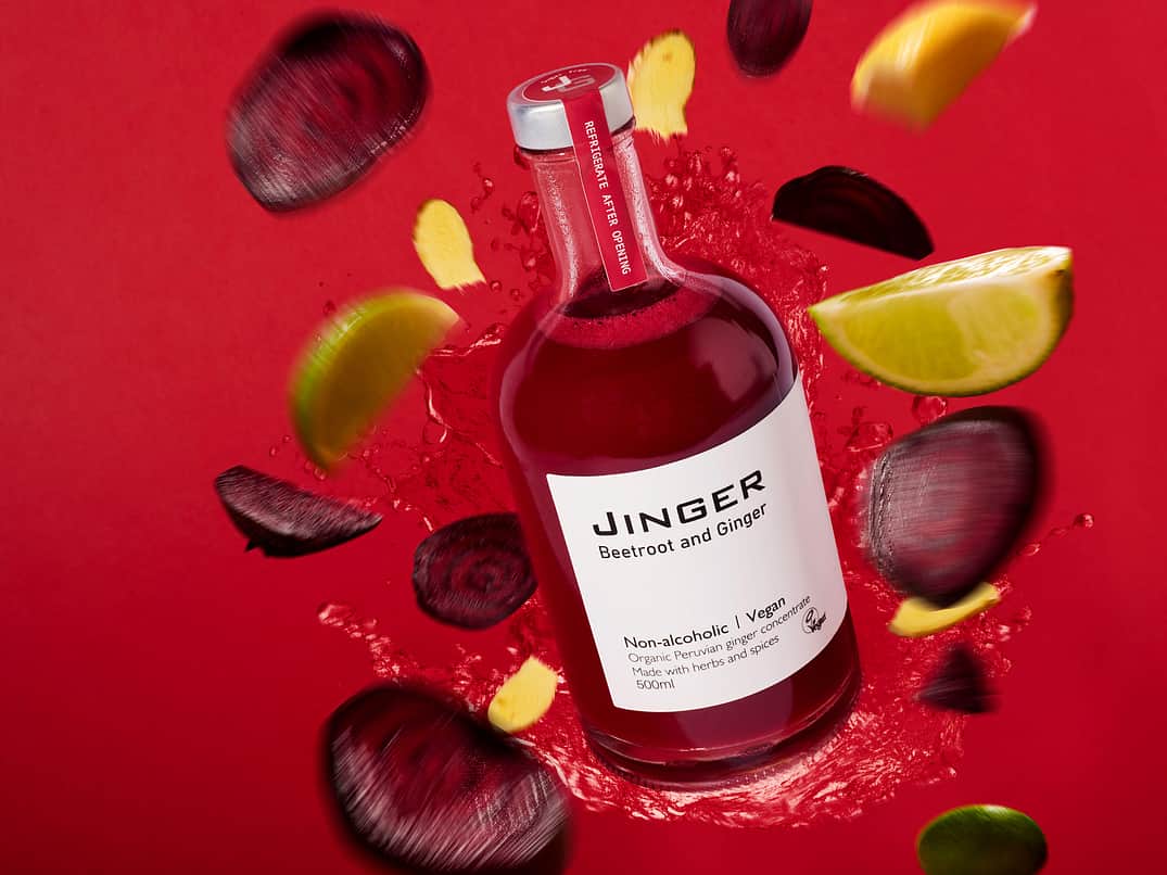 Bottle of beetroot and ginger juice on a red background with sliced beetroot and fresh citrus pieces, highlighting premium beverage packaging, natural ingredients, and food and drink branding.