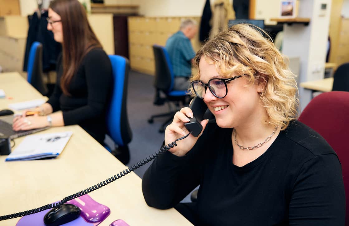 A smiling woman in an office, talking on the telephone.