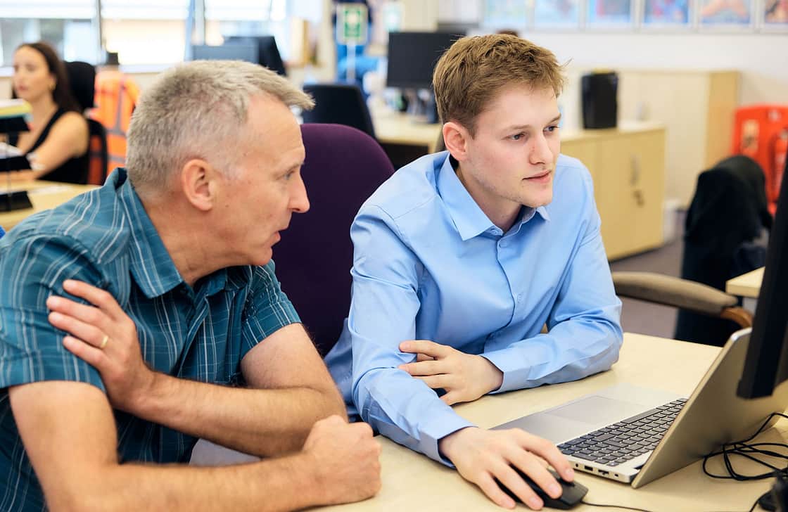 Two People Infront of a PC discussing work on a screen in an office environment.