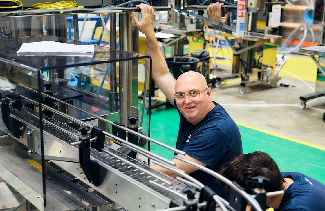 Adelphi 0506 Happy man looking friendly into the camera smiling while next to a production machine