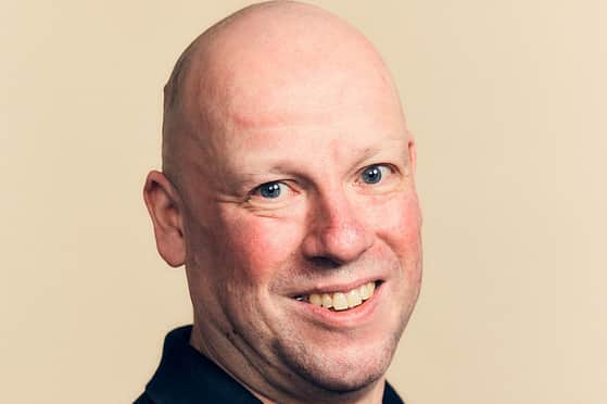 A smiling man wearing a navy blue Adelphi T-Shirt.