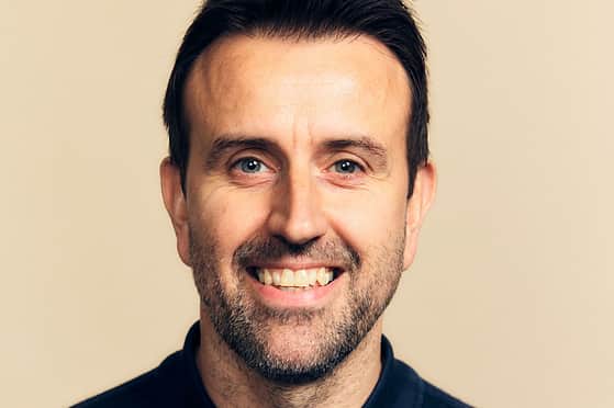 Headshot of a smiling man with short dark hair, and a beard, wearing a dark navy polo shirt.