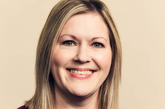 A smiling woman with shoulder length blonde hair, wearing a burgundy top.