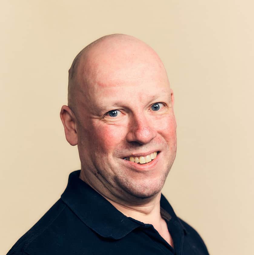 A smiling man wearing a navy blue Adelphi T-Shirt.