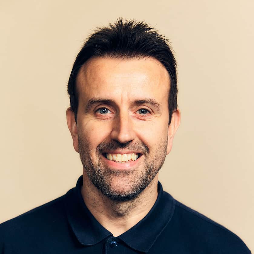 Headshot of a smiling man with short dark hair, and a beard, wearing a dark navy polo shirt.