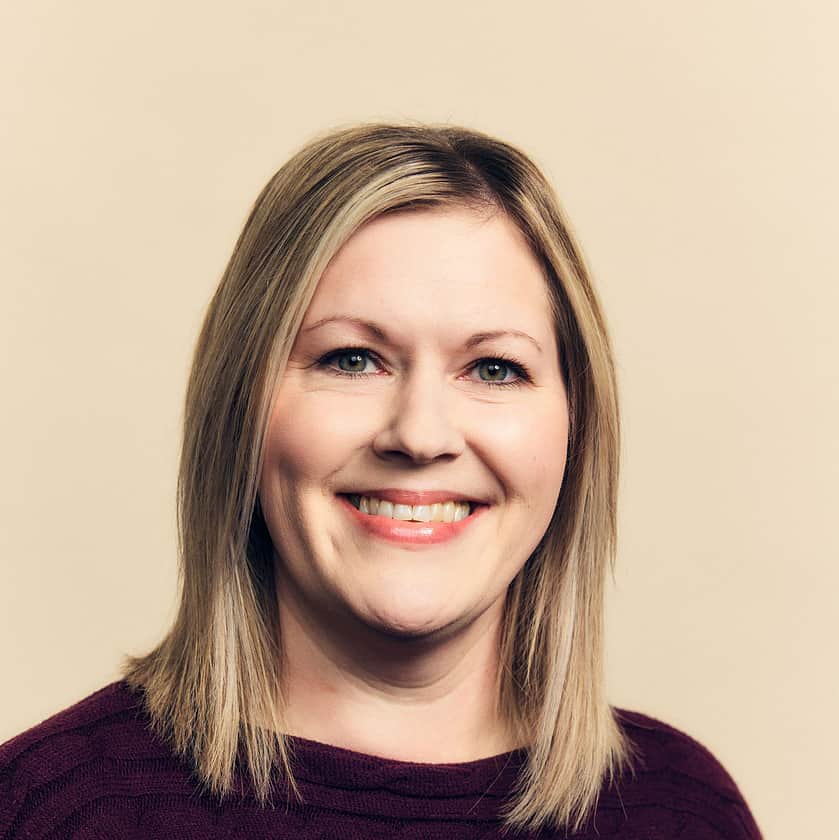 A smiling woman with shoulder length blonde hair, wearing a burgundy top.